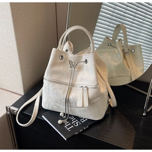 Detail of cream bucket bag with silver butterfly charm and pearl drawstrings