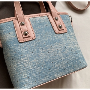Detail of light blue denim bucket bag with silver studs and pink leather strap handles