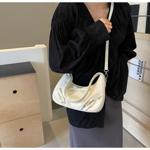 Detail of white handbag with 3D bow accents and adjustable strap on a model