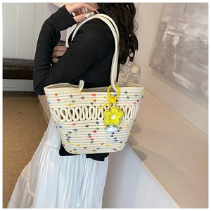 Détail d'un sac cabas tissé beige avec pompons colorés et breloque fleur jaune