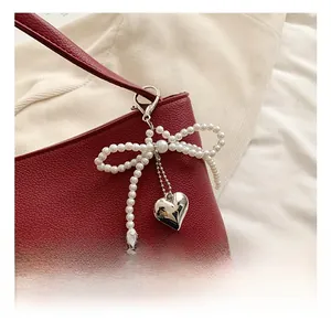 Detail of white pearl bow and silver heart pendant on red leather handbag