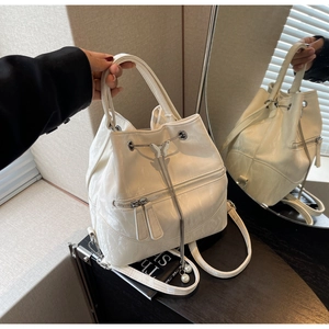 Detail of off-white glossy bucket bag featuring metallic butterfly charm and drawstring