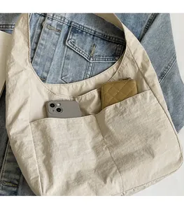 Detalle de un bolso tote de nailon crema con dos bolsillos frontales y asa ancha