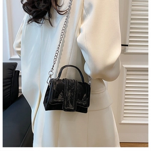 Detail of a mini black crossbody bag with marble texture and silver chain strap