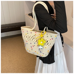 Détail du sac cabas tissé avec pompons colorés et accessoire de charme fleur jaune