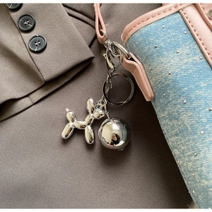 Detail view of silver mirror balloon dog charm and ball pendant on blue denim bucket bag
