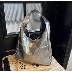 Détail du sac cabas métallisé argenté avec texture plissée sur marbre avec un livre