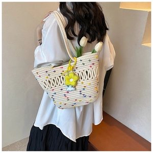 Détail d'un sac cabas tissé beige avec pompons colorés et breloque florale porté à l'épaule