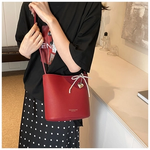 Detail of red bucket bag with pearl bow and heart charm on a crossbody strap