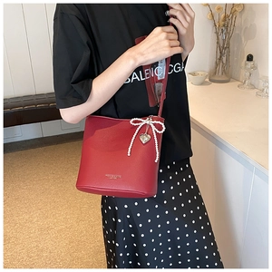 Detail of red leather bucket bag featuring a pearl bow charm and heart-shaped pendant