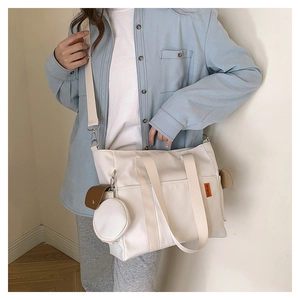 Detail view of large white nylon tote bag with orange label and round mini purse charm