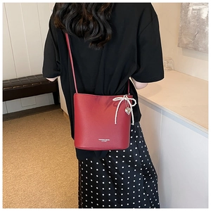 Detail of red PU leather bucket bag featuring a pearl bow and heart pendant charm