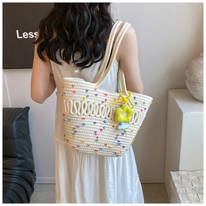Détails d'un sac cabas tissé blanc orné de pois colorés et d'un pendentif fleur de soleil