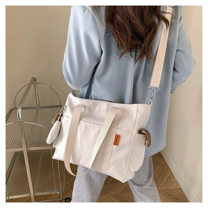 Detail view of cream canvas tote bag with wide strap and mini pouch on model side