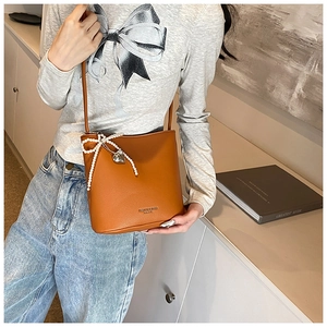 Close-up of caramel bucket bag with pearl bow and heart pendant in casual setting