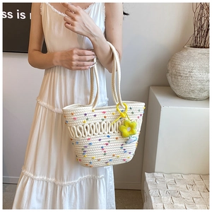 Détail du sac tissé avec des pompons colorés et un accessoire charm de fleur jaune