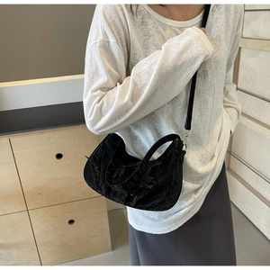 Detail of black embossed crescent bag featuring a bow and slim leather strap on shoulder