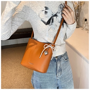 Detail of orange bucket bag with lychee texture and pearl bow charm on model