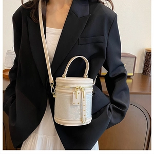 Detailed view of beige embroidered bucket bag worn crossbody by a model in casual setting