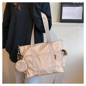Detail of beige nylon tote bag featuring front pocket, orange label, and mini round pouch