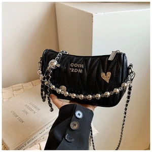 Detail of black quilted crossbody bag with silver heart charm and pearly chain strap