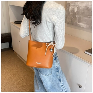 Brown orange bucket bag with pearl bow and heart charm detail shown on model