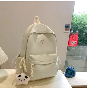 Detail of cream white backpack featuring a small bear logo and star plush charm accessory