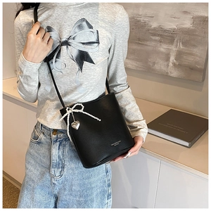 Detail of black leather bucket bag featuring pearl bow and silver heart pendant decoration