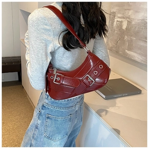 Detail of burgundy glossy leather shoulder bag with silver buckles and grommet straps