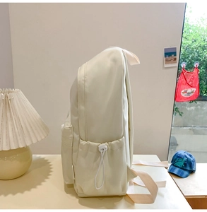 Detail of minimalist cream nylon backpack side pocket with adjustable drawstring