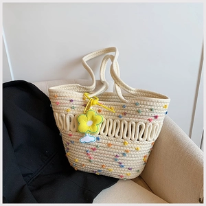 Détail d'un sac cabas tissé beige avec pompons colorés et charm de fleur jaune