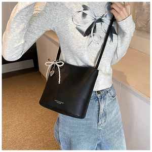 Detail of black lychee leather bucket bag featuring pearl bow charm and silver heart pendant