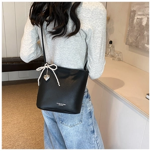 Close-up of black litchi leather bucket bag with pearl bow and silver heart pendant