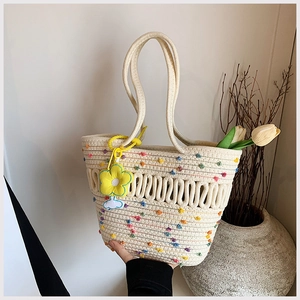 Détail du sac de plage tissé avec pompons colorés, motif ajouré et breloque fleur jaune