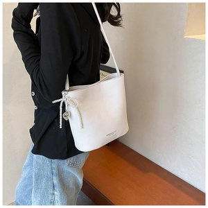 Detail of white lychee leather bucket bag with pearl bow and metal heart pendant