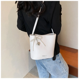 White lychee leather bucket bag with pearl bow detail and heart pendant on a shoulder strap