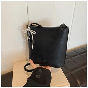 Close-up of black litchi grain bucket bag featuring a pearl bow charm and heart pendant
