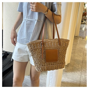 Detail of hand-woven beige straw tote bag with brown leather handles and square patch
