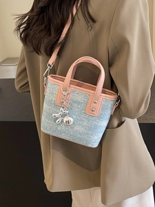 Contrast color bucket bag in blue tweed and pink leather shown on a shoulder