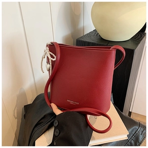 Close-up of wine red bucket bag featuring pebble leather and pearl bow charm detail