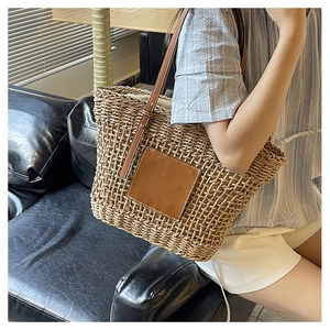 Detail of straw woven tote bag featuring brown leather patch and shoulder straps