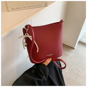 Close-up of burgundy bucket bag with pearl bow charm and litchi grain leather texture