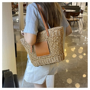 Detail of hand-woven straw tote with brown leather patch and long shoulder straps
