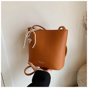 Detail of brown litchi leather bucket bag with pearl bow and silver heart charm