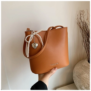 Detail of orange-brown bucket bag with pearl bow, metal heart charm and embossed text