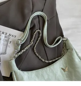 Detail of mint green tote bag featuring silver butterfly ornament and wrinkled leather texture