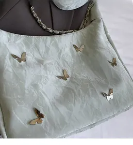 Detail of mint green crinkled tote bag featuring silver butterfly accents and chain strap