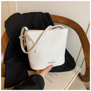 Detail of white bucket bag with pearl heart pendant and fashion text on dark wood chair