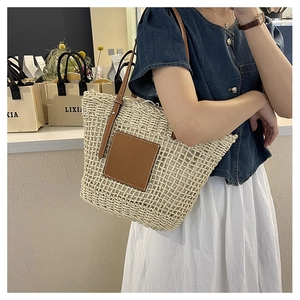 Detail of cream woven tote bag featuring brown leather patch and shoulder straps