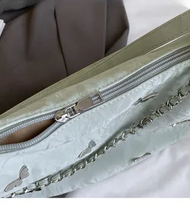 Detailed close-up of smooth metal zipper and silver bird ornaments on soft green tote bag